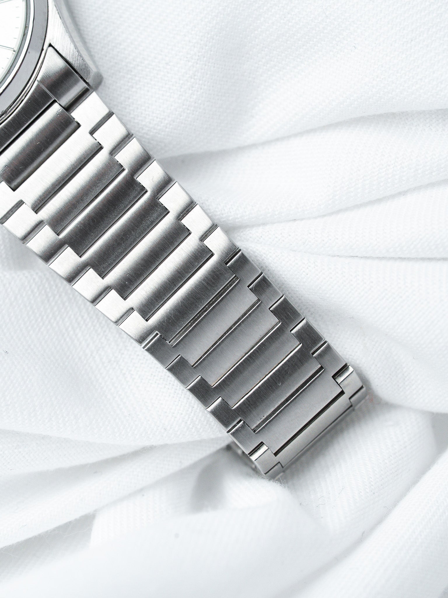 Vintage Omega watch with brushed steel bracelet on white fabric background