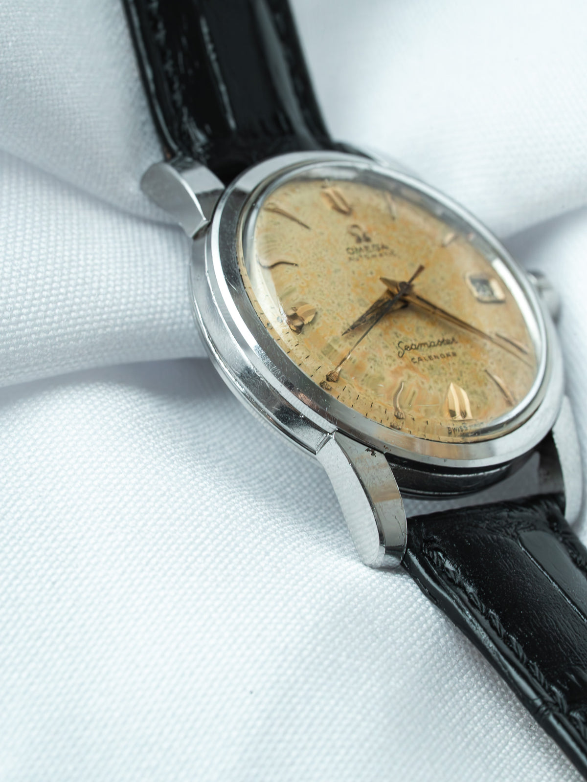 Vintage Omega Seamaster Calendre watch with aged dial, steel case, black leather strap on white fabric