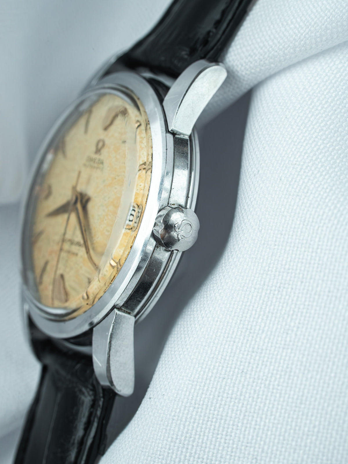 Vintage Omega watch with cream dial, steel case, black leather strap on white fabric