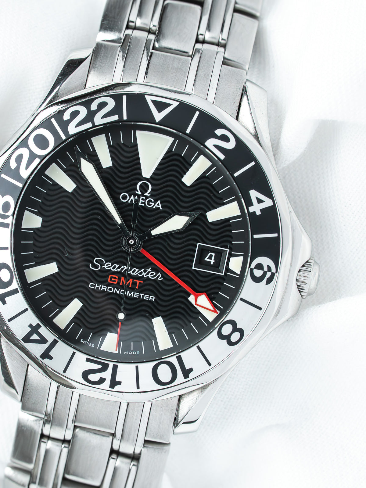 Omega Seamaster GMT Chronometer watch with black wavy dial, red GMT hand, and steel bracelet