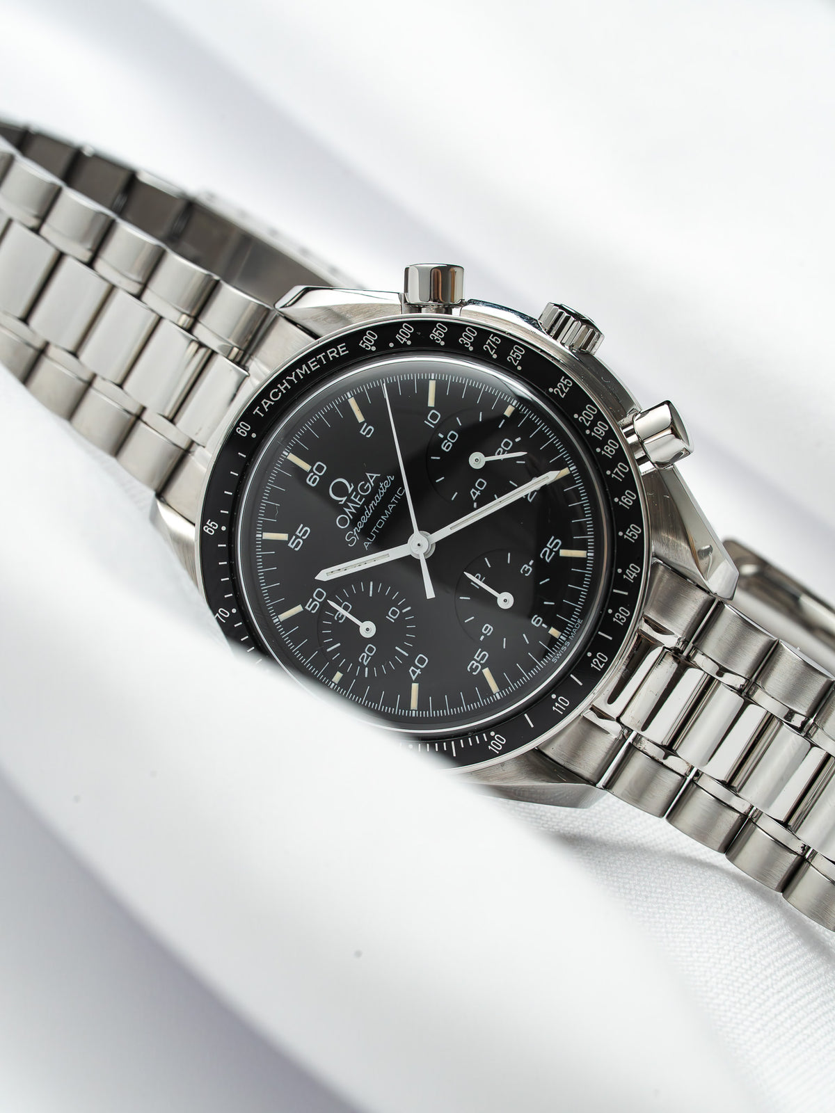 Omega Speedmaster Automatic chronograph with black dial, steel bracelet, tachymeter bezel on white background