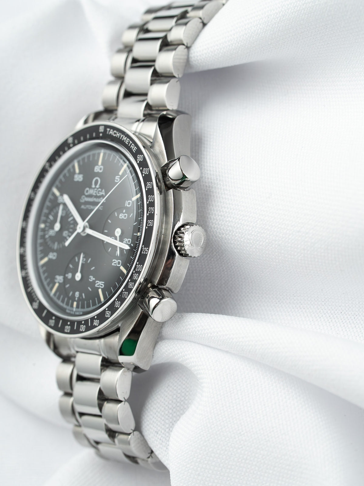 Omega Speedmaster chronograph with black dial, tachymeter bezel, and steel bracelet on white fabric