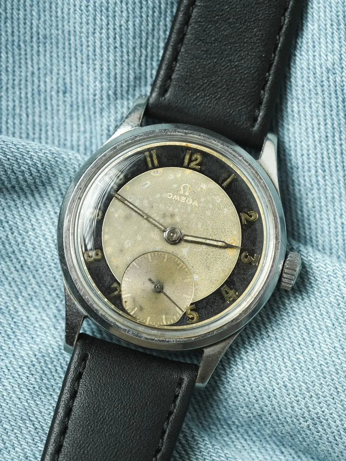 Vintage Omega watch with silvered dial, black chapter ring, and black leather strap on denim