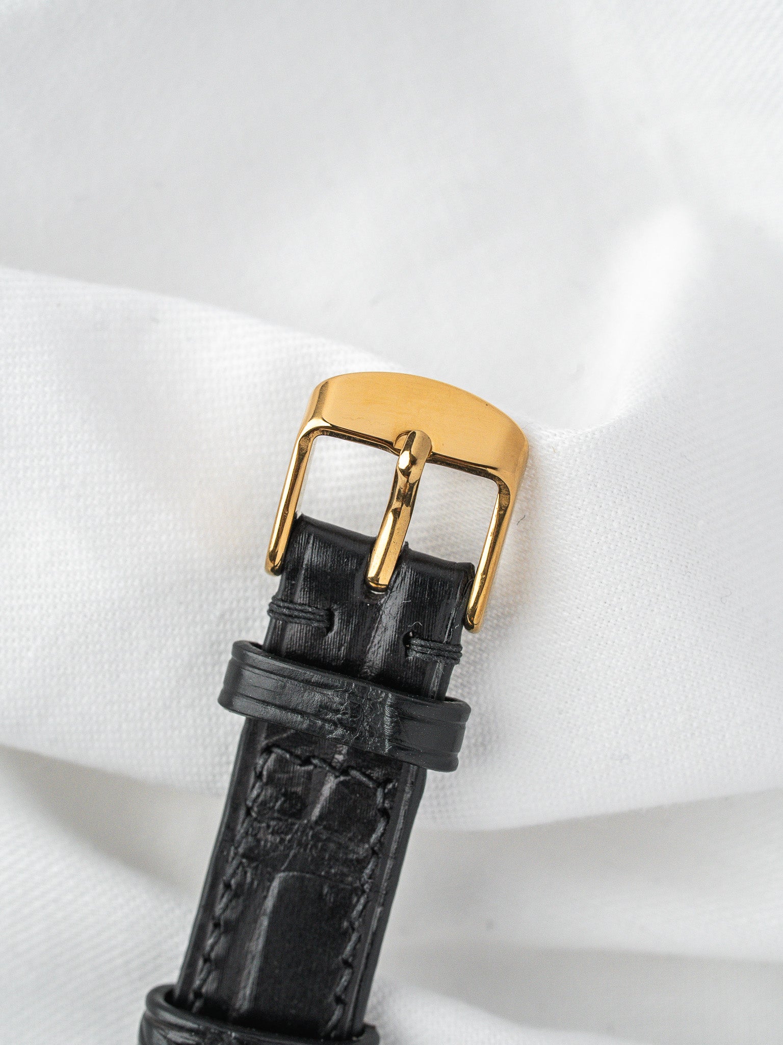 Black alligator leather watch strap with gold buckle on white fabric