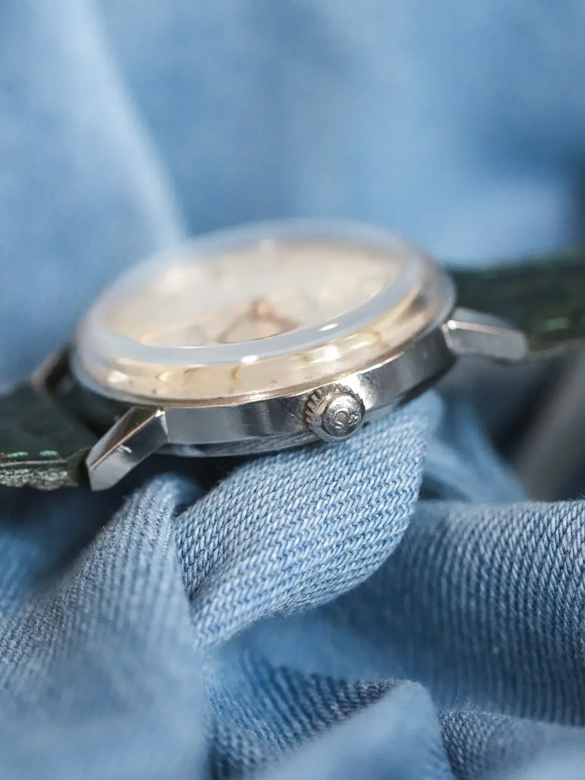 Vintage Omega watch with silver case, cream dial, green strap on denim