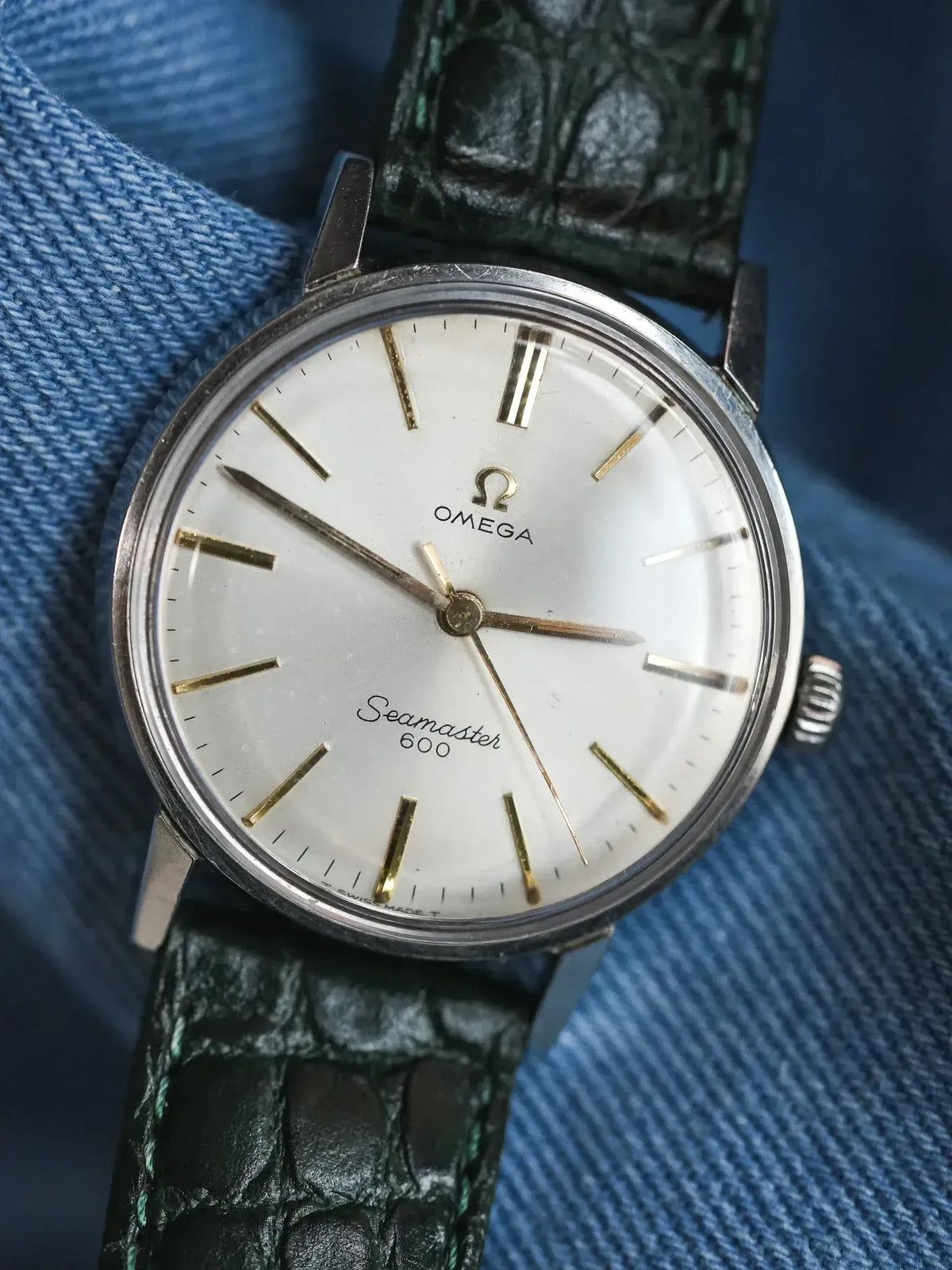 Vintage Omega Seamaster 600 watch with white dial, gold markers, green alligator strap on denim