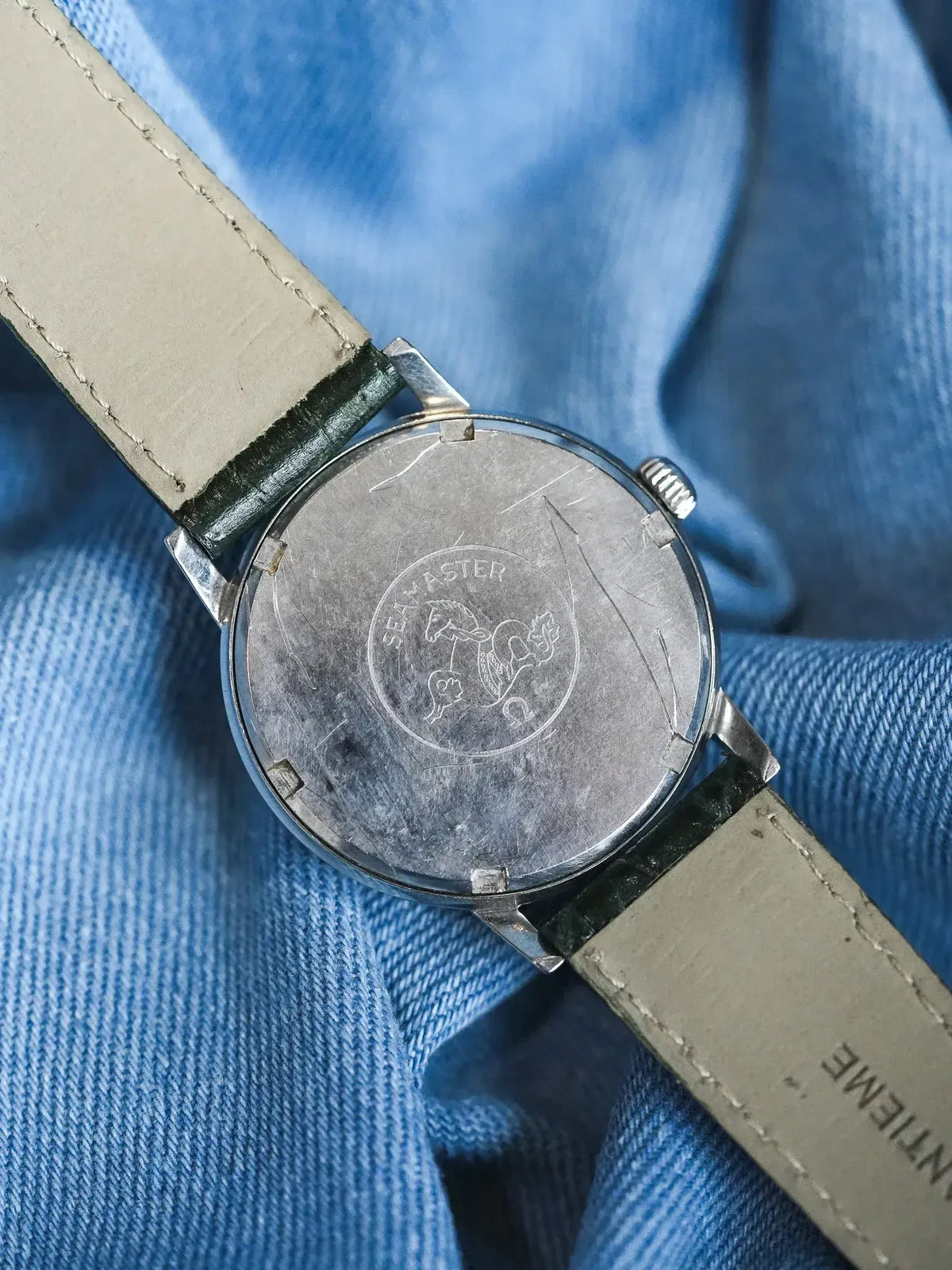 Vintage Omega Seamaster watch back with engraved logo, steel case, green leather strap on denim