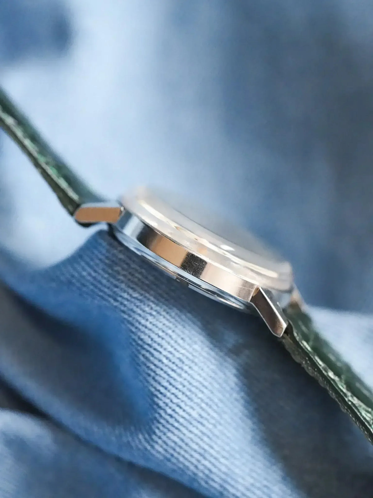 Vintage Omega watch with green leather strap, silver case on blue fabric