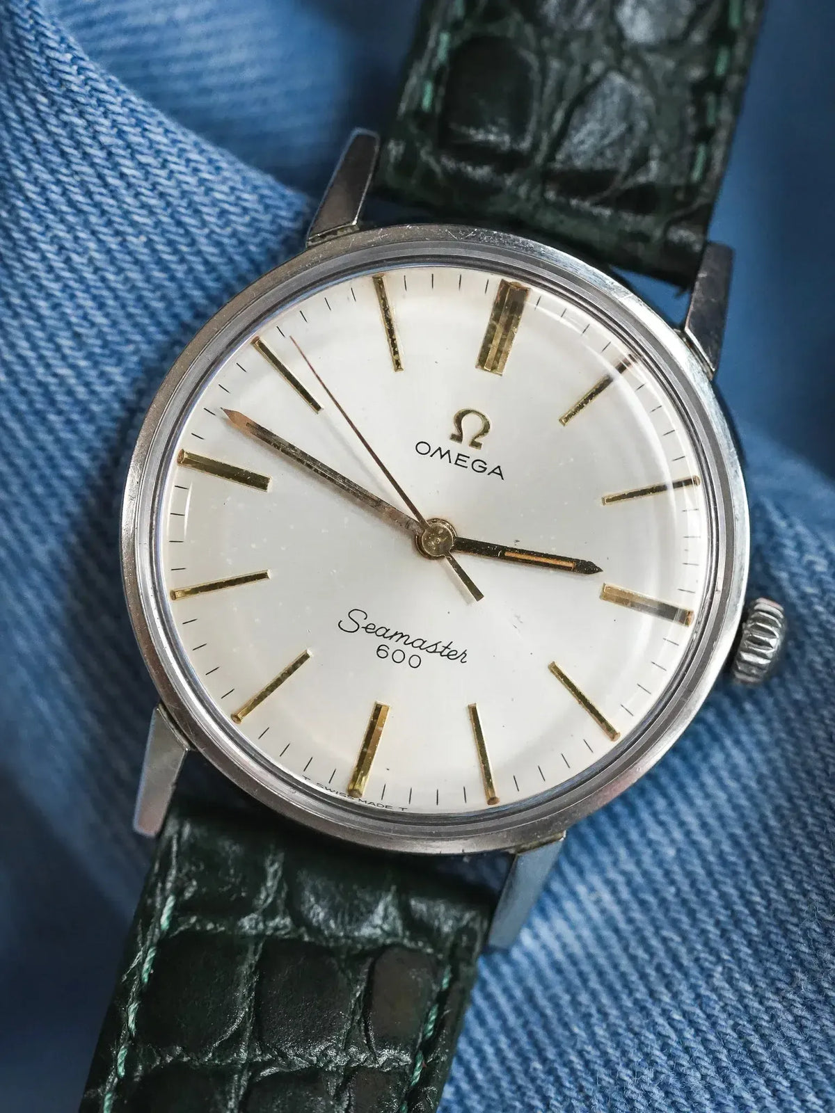 Vintage Omega Seamaster 600 watch with white dial, gold markers, green crocodile strap on denim