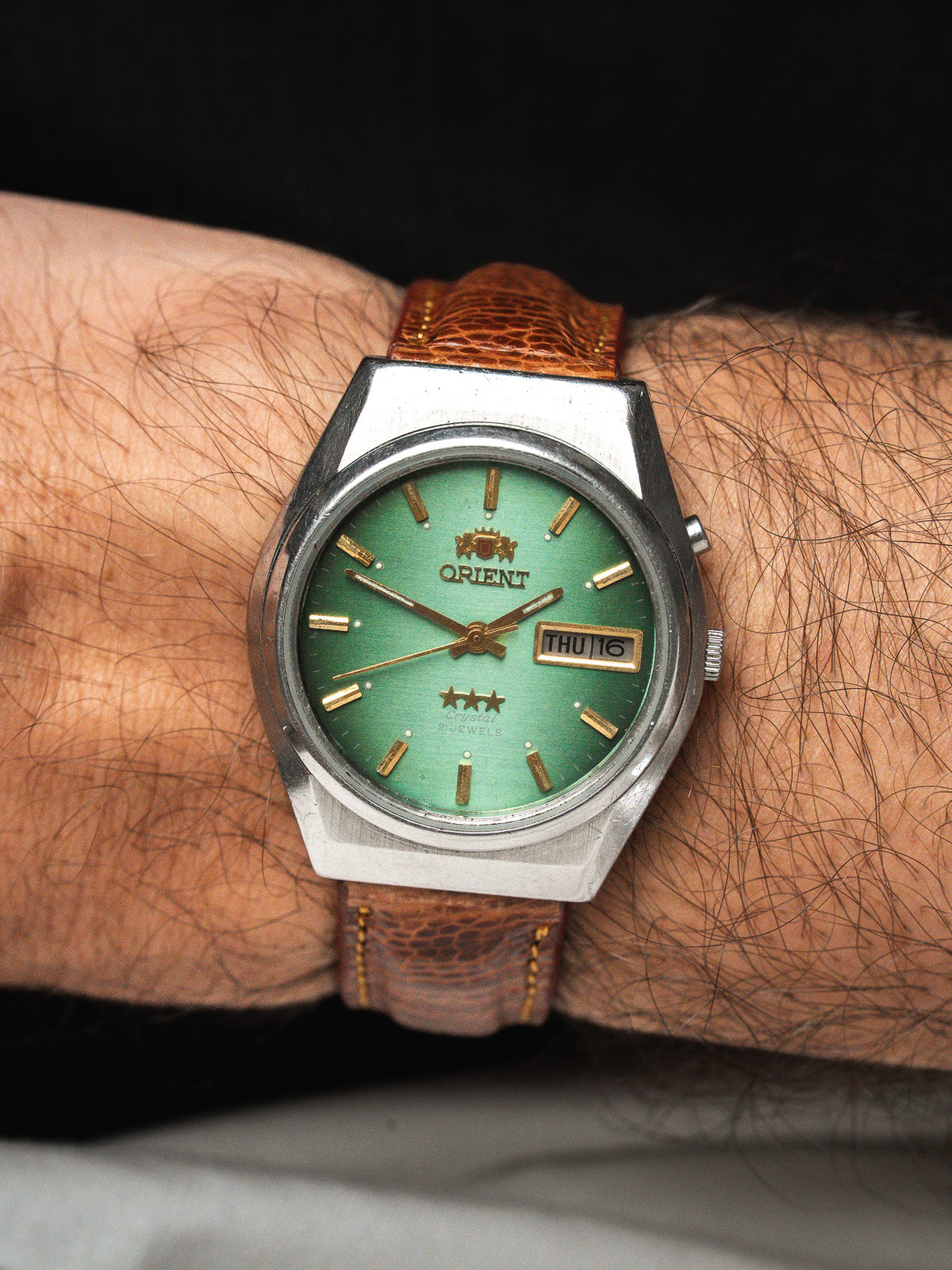 Montre Orient vintage au cadran vert et bracelet en cuir marron portée au poignet