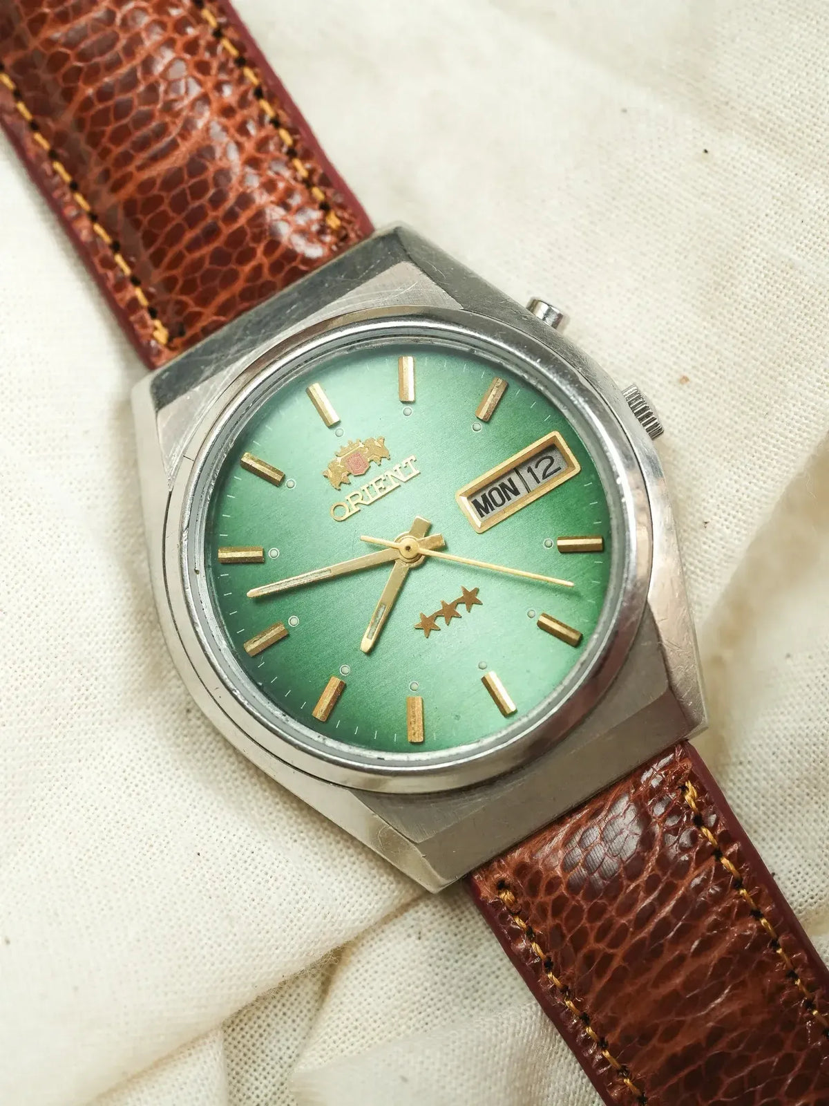 Orient vintage watch with green dial, gold markers, and brown leather strap on fabric
