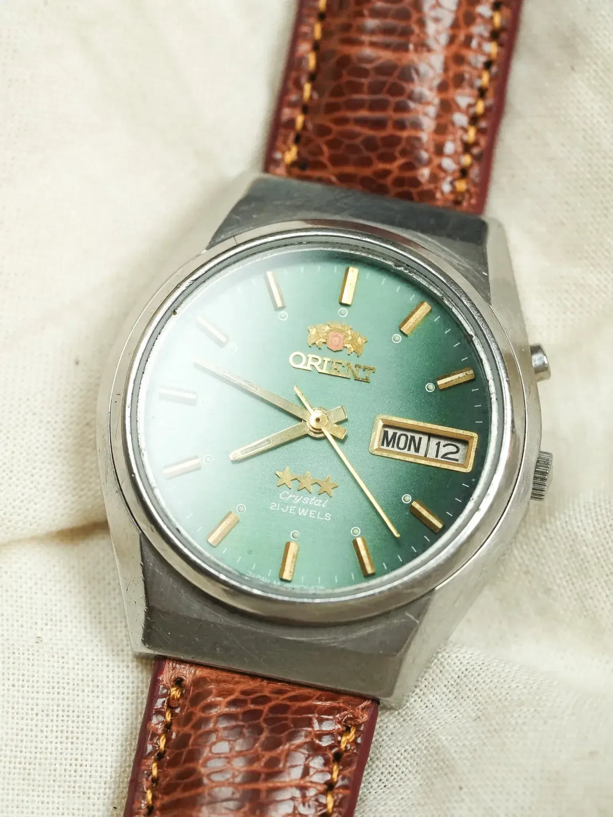 Orient vintage watch with green gradient dial, gold markers, brown leather strap on textured fabric