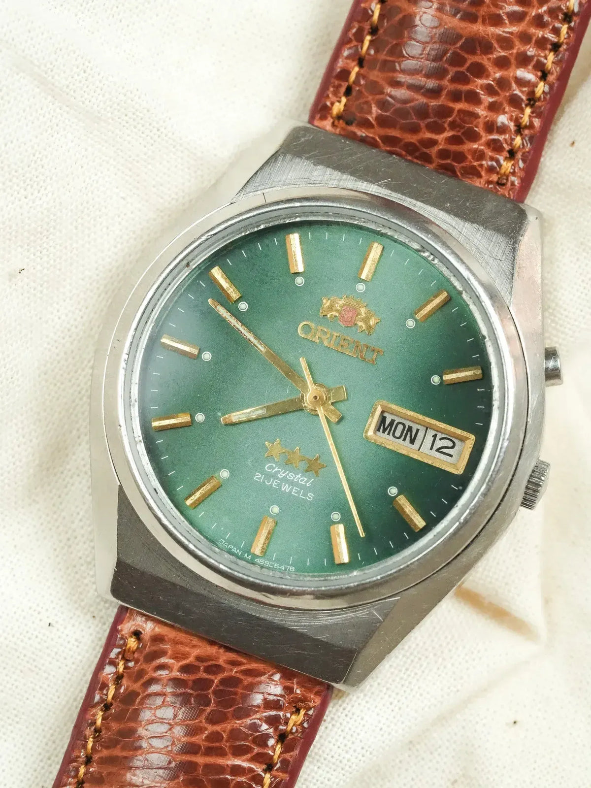 Orient vintage watch with green dial, gold markers, brown leather strap on white fabric