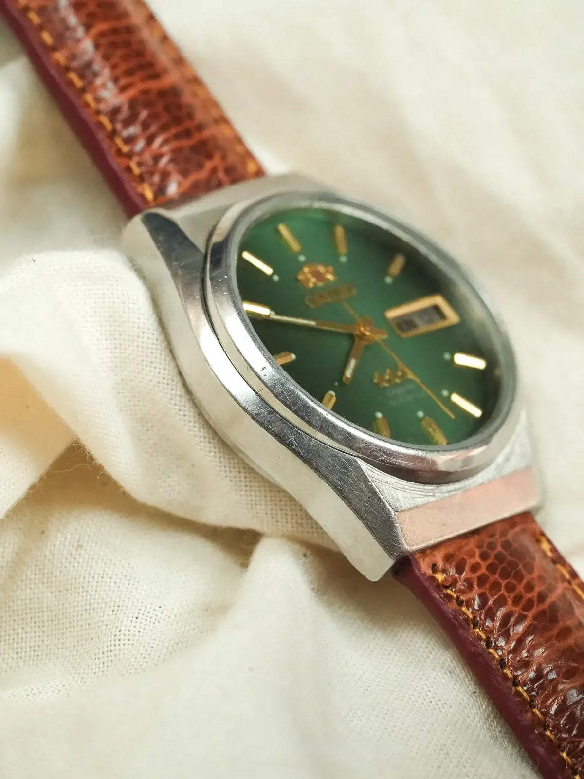 Vintage Seiko watch with green dial, gold markers, and brown leather strap on fabric
