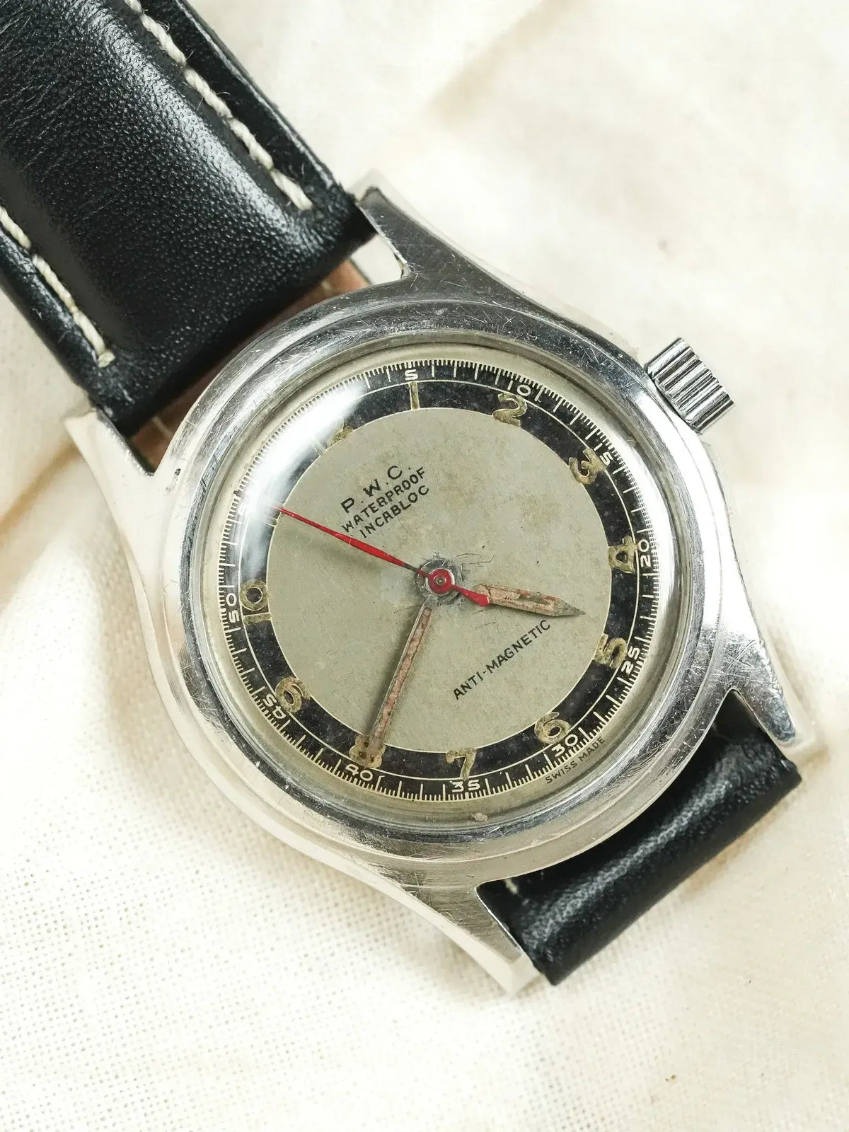 P.W.C. vintage watch with silver dial, black bezel, red second hand, leather strap