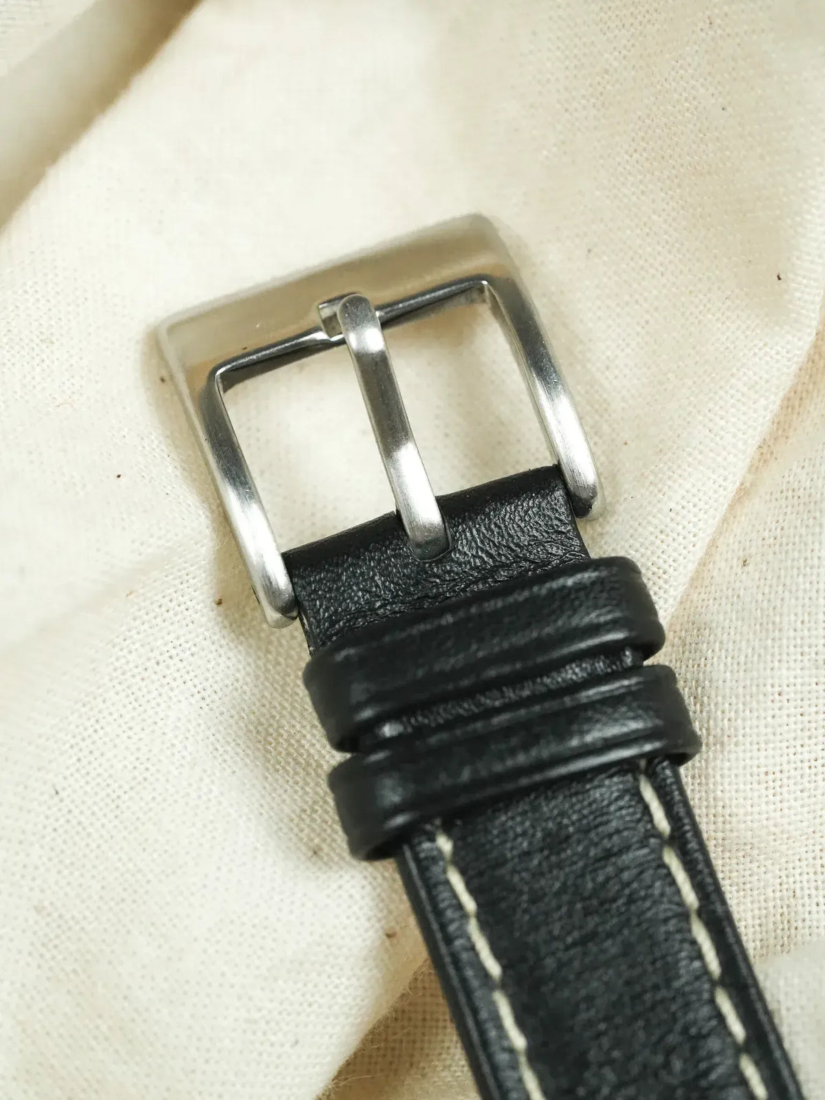 Black leather watch strap with white stitching and silver buckle