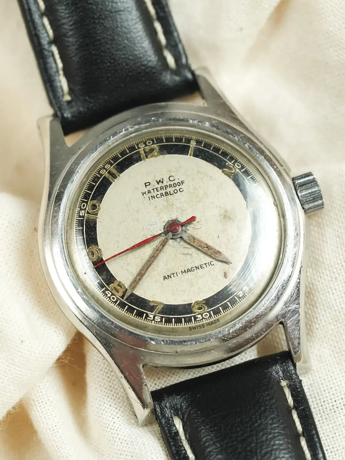 P.W.C. vintage watch with silver case, cream dial, black leather strap, red seconds hand