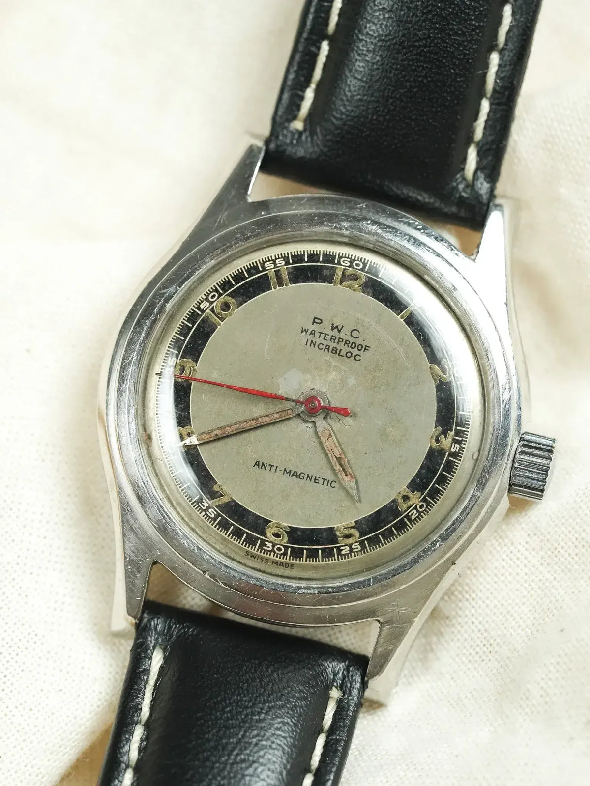 P.W.C. vintage watch with silver dial, black bezel, red second hand, and black leather strap