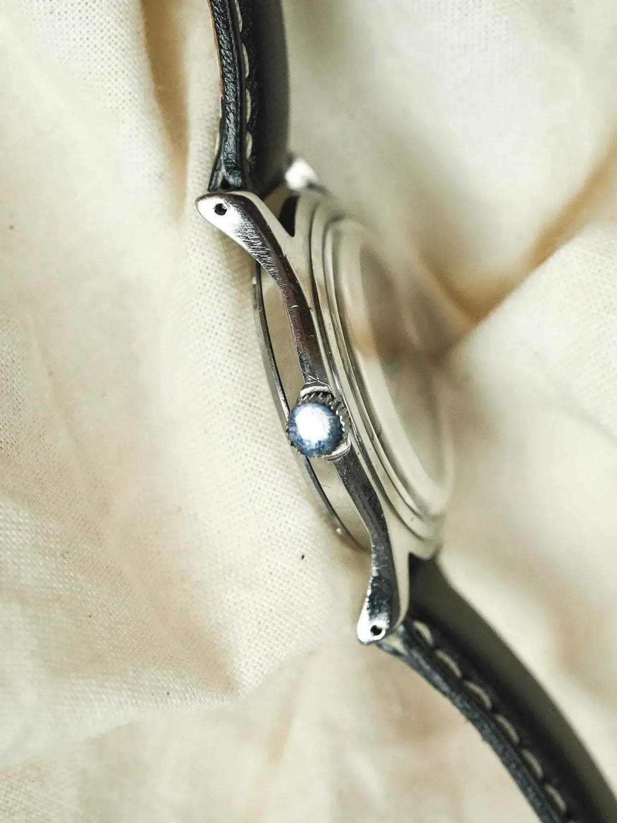 Vintage watch with black leather strap and silver case on fabric