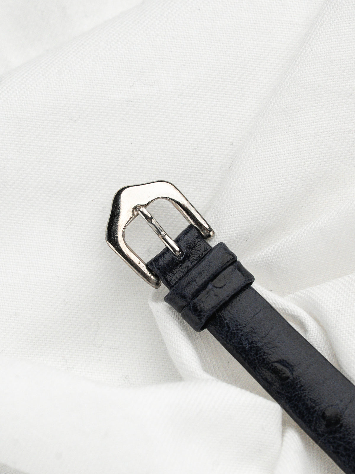 Détail du fermoir argenté et du bracelet en cuir noir grainé sur fond blanc.