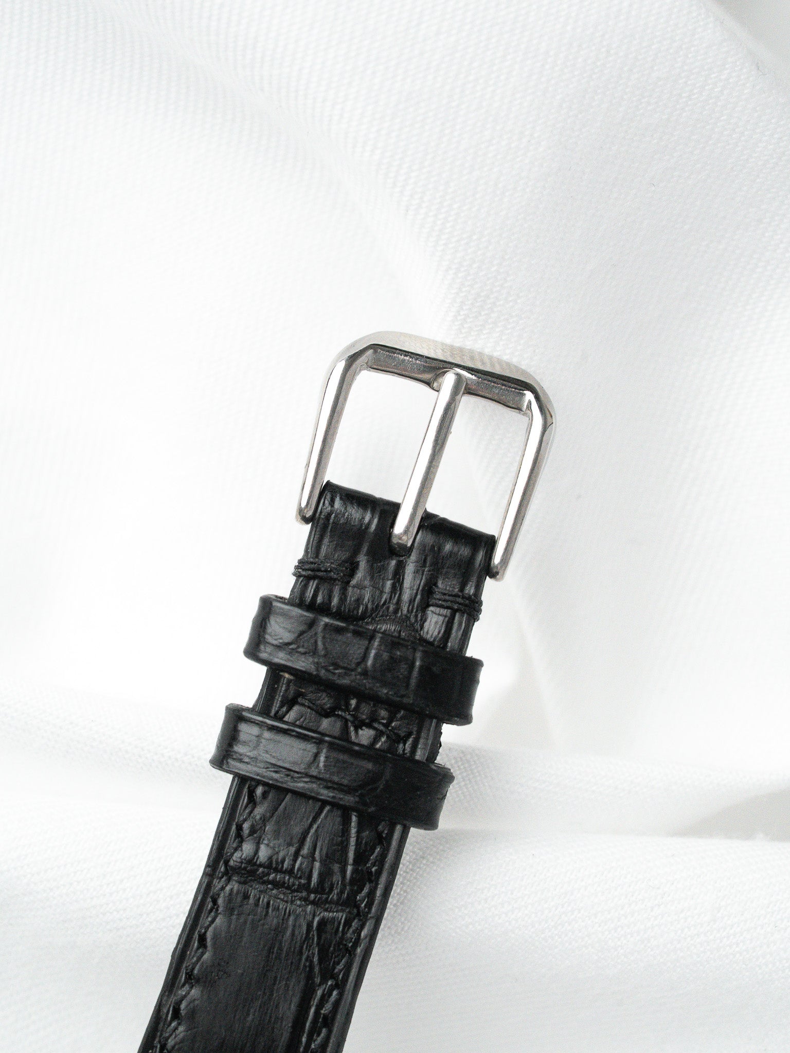 Black alligator leather watch strap with silver buckle on white fabric