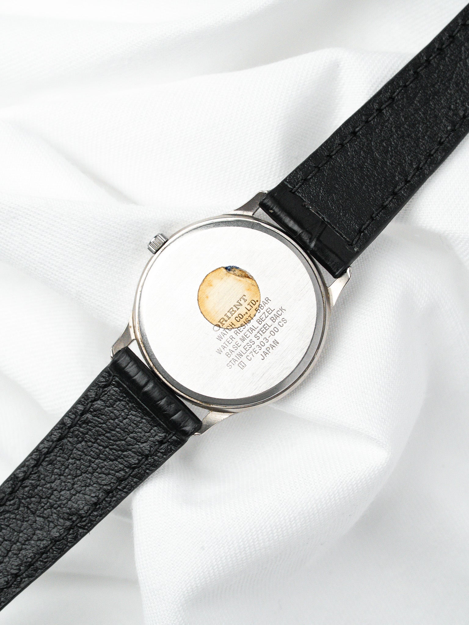 Orient vintage watch with stainless steel case and black leather strap, back view on white fabric