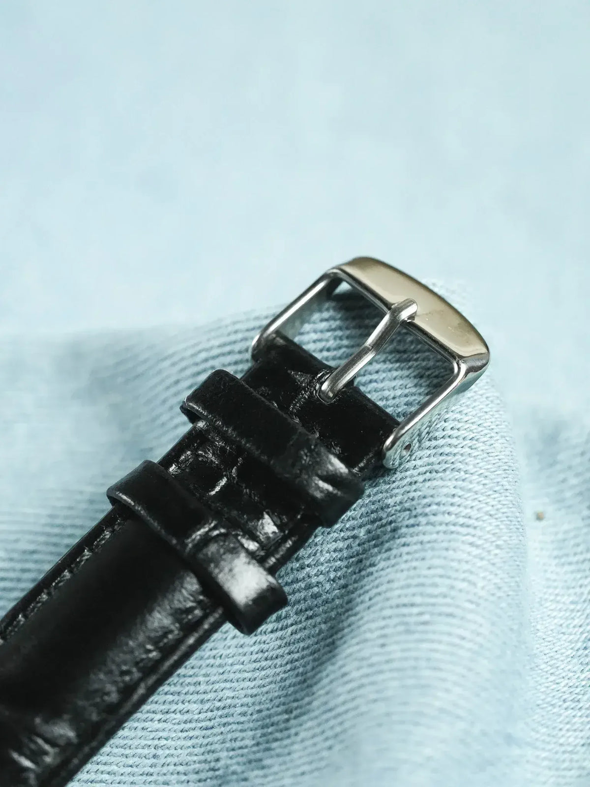 Black leather watch strap with silver buckle on denim background