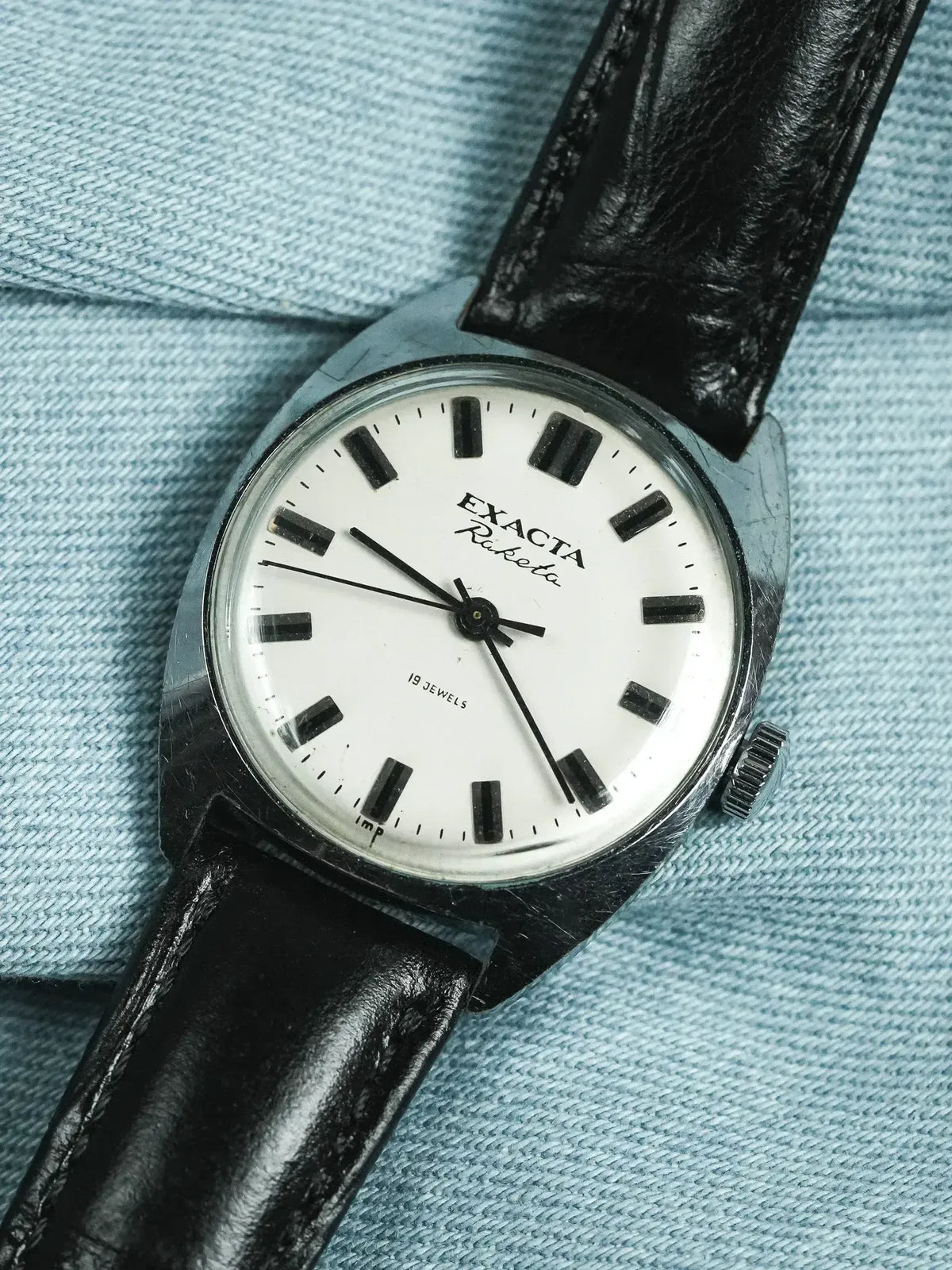 Exacta Raketa vintage watch with white dial, black markers, and leather strap on denim