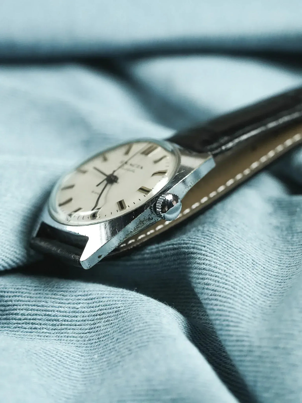 Omega vintage watch with silver case, cream dial, black leather strap on fabric