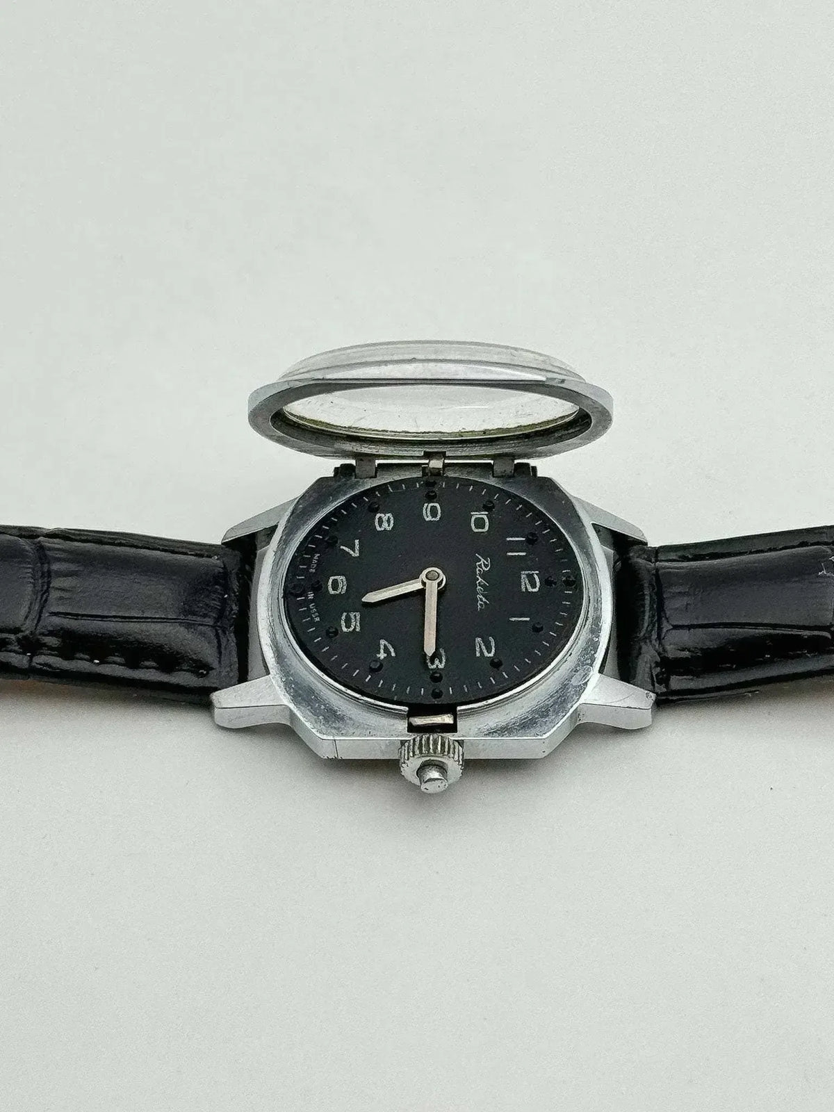 Vintage Raketa watch with black dial, steel case, and black leather strap, displayed open on white background