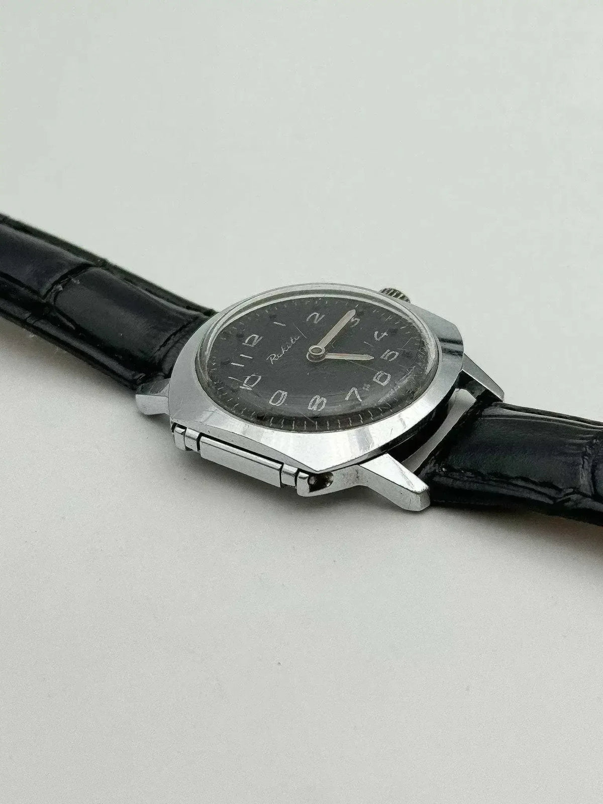 Raketa vintage watch with black dial, silver case, and black leather strap on neutral background