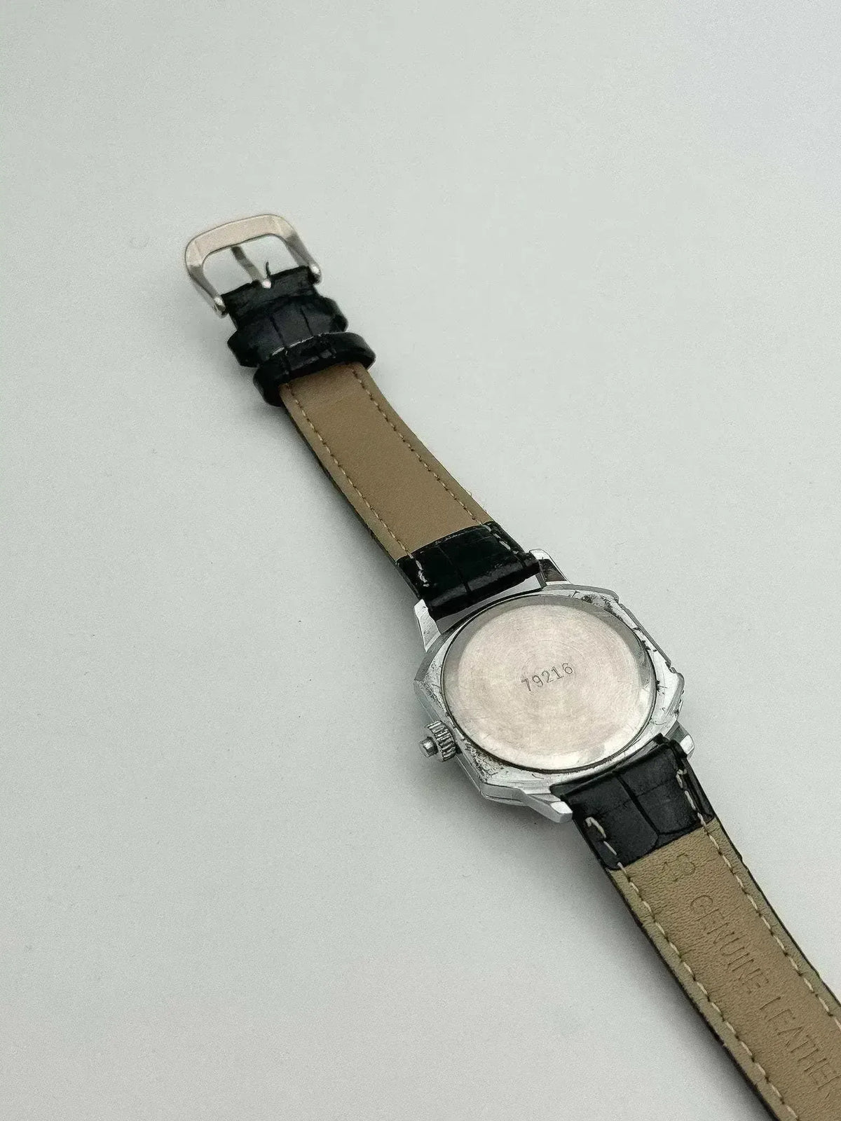 Vintage Universal Genève watch with black leather strap, silver case back, on neutral background