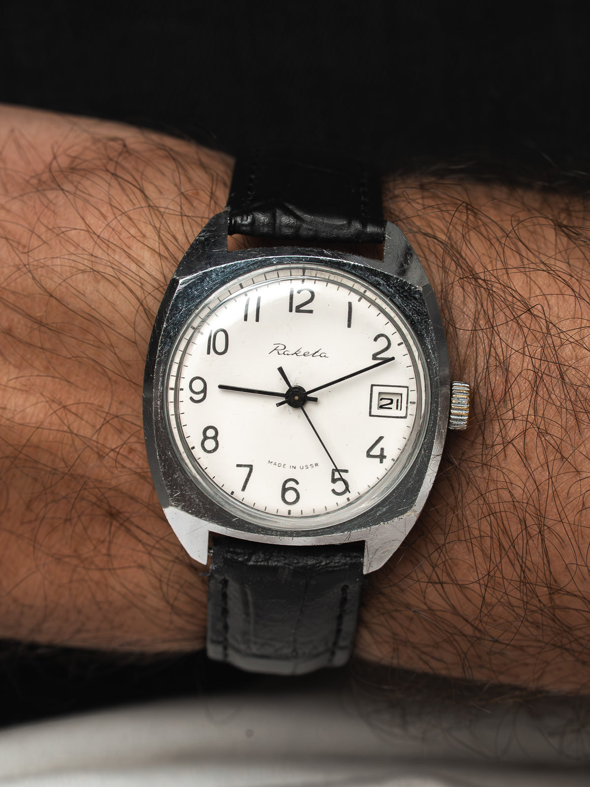 Montre Raketa vintage au boîtier acier, cadran blanc et bracelet cuir noir, au poignet