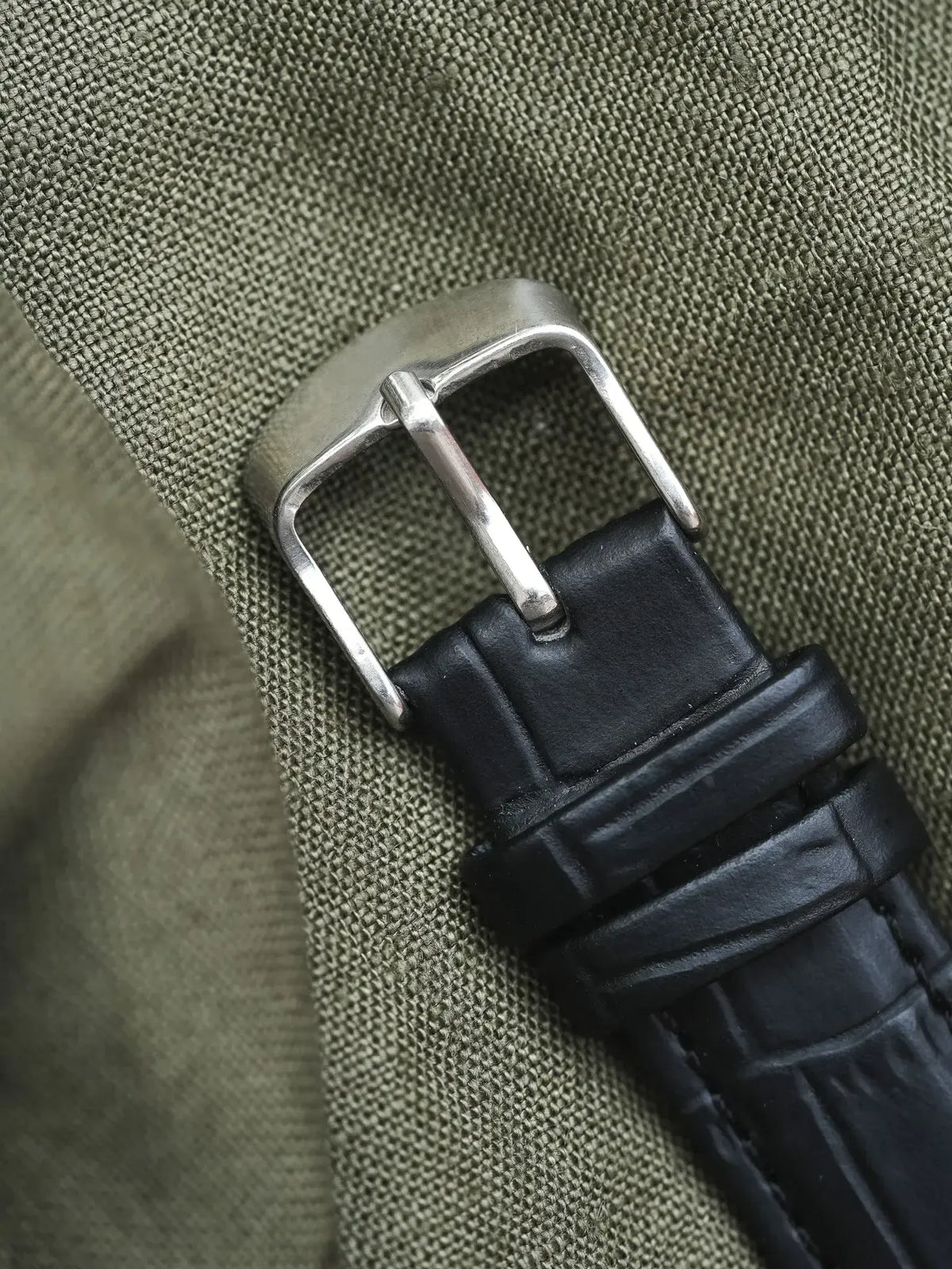 Black leather watch strap with silver buckle on olive fabric