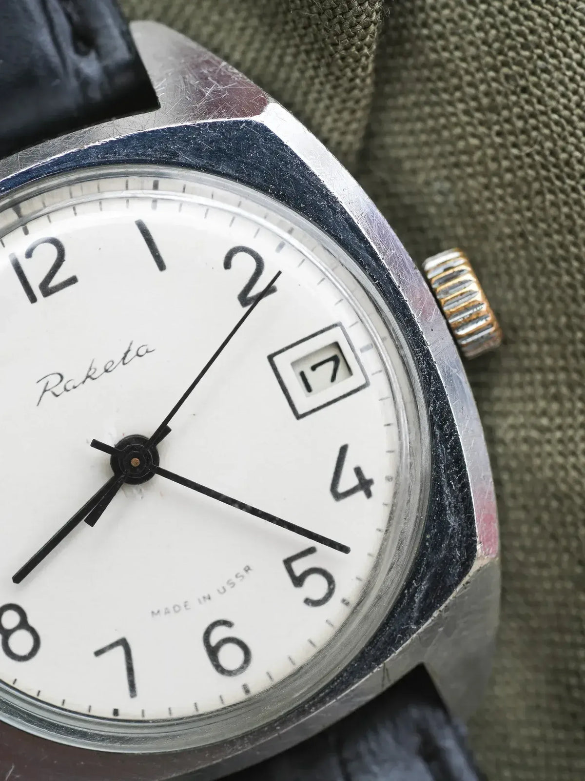 Raketa vintage watch with white dial, black numerals, and date window on olive fabric