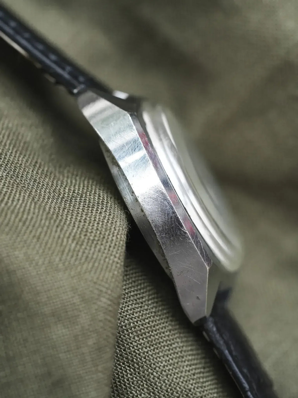 Vintage Omega watch side profile, stainless steel case, black leather strap on olive fabric