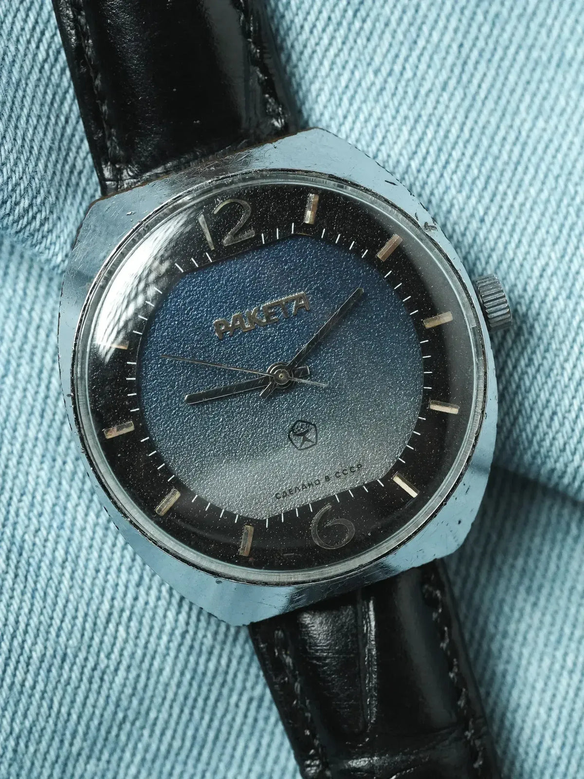Vintage Raketa watch with blue gradient dial, steel case, black leather strap on denim