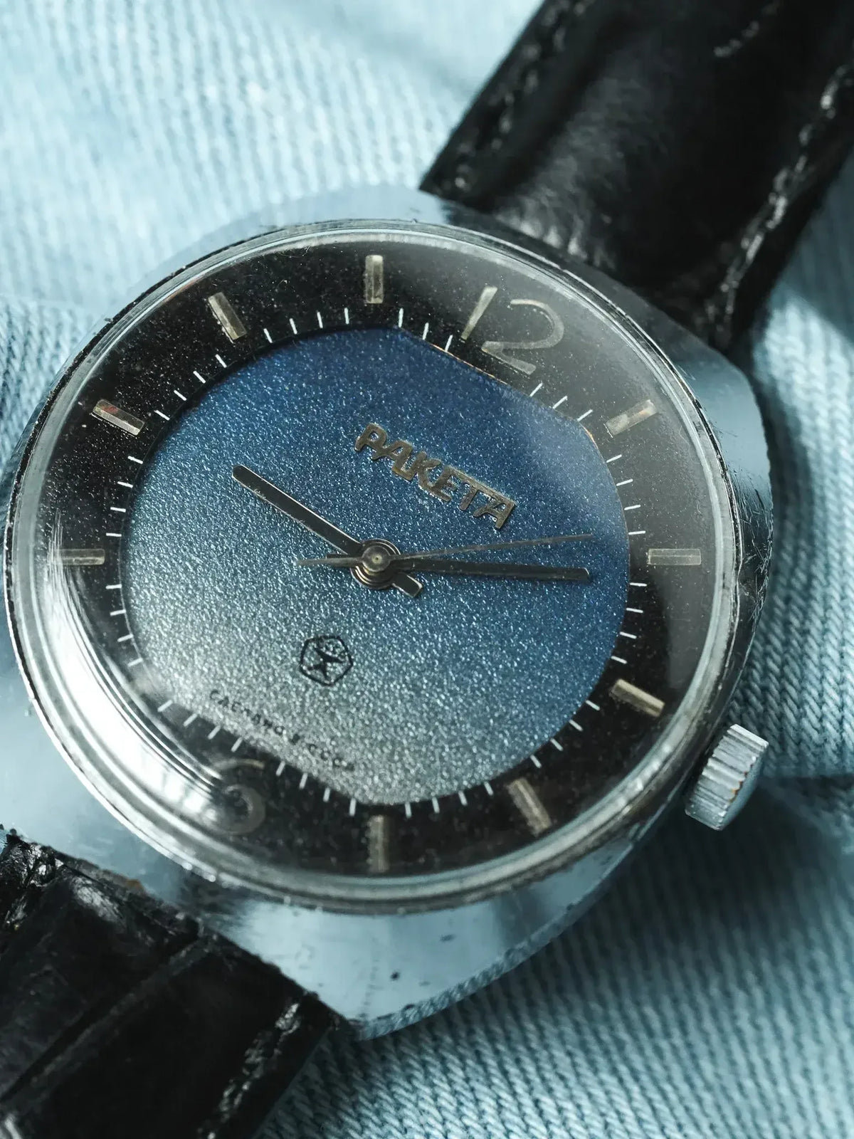 Vintage Raketa watch with blue textured dial, black leather strap, steel case on denim