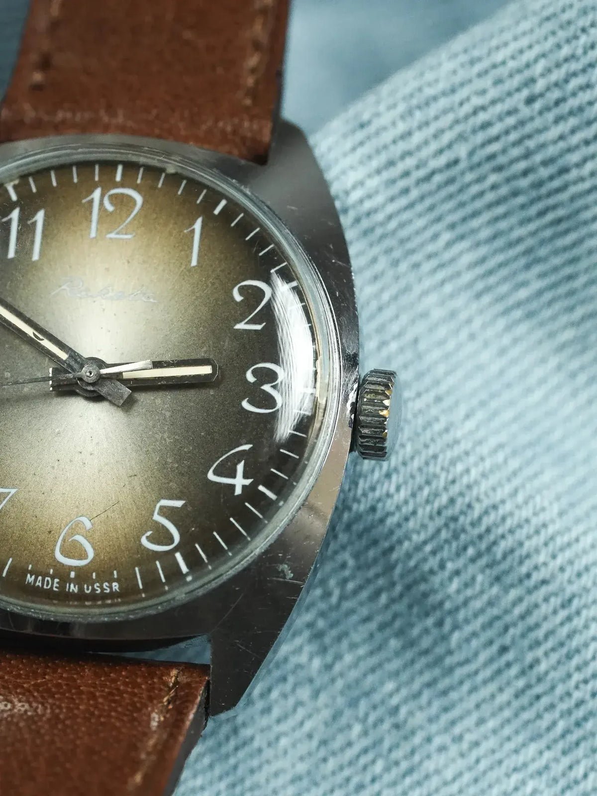Raketa vintage watch with dark dial, white numerals, brown leather strap on denim