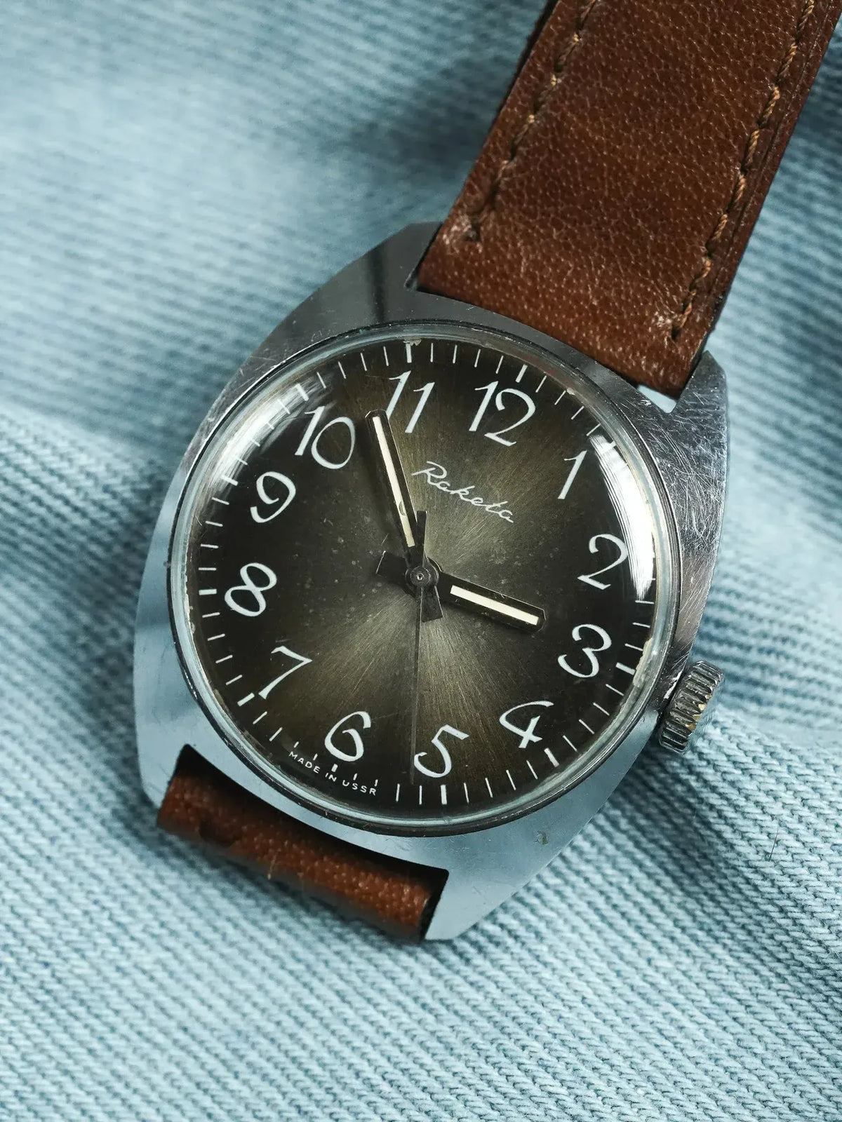Raketa vintage watch with black dial, white numerals, brown leather strap on denim