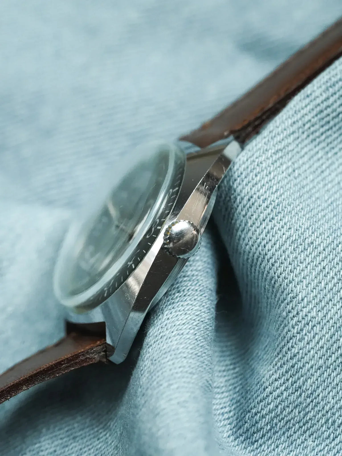 Vintage Omega watch with steel case and brown leather strap on denim