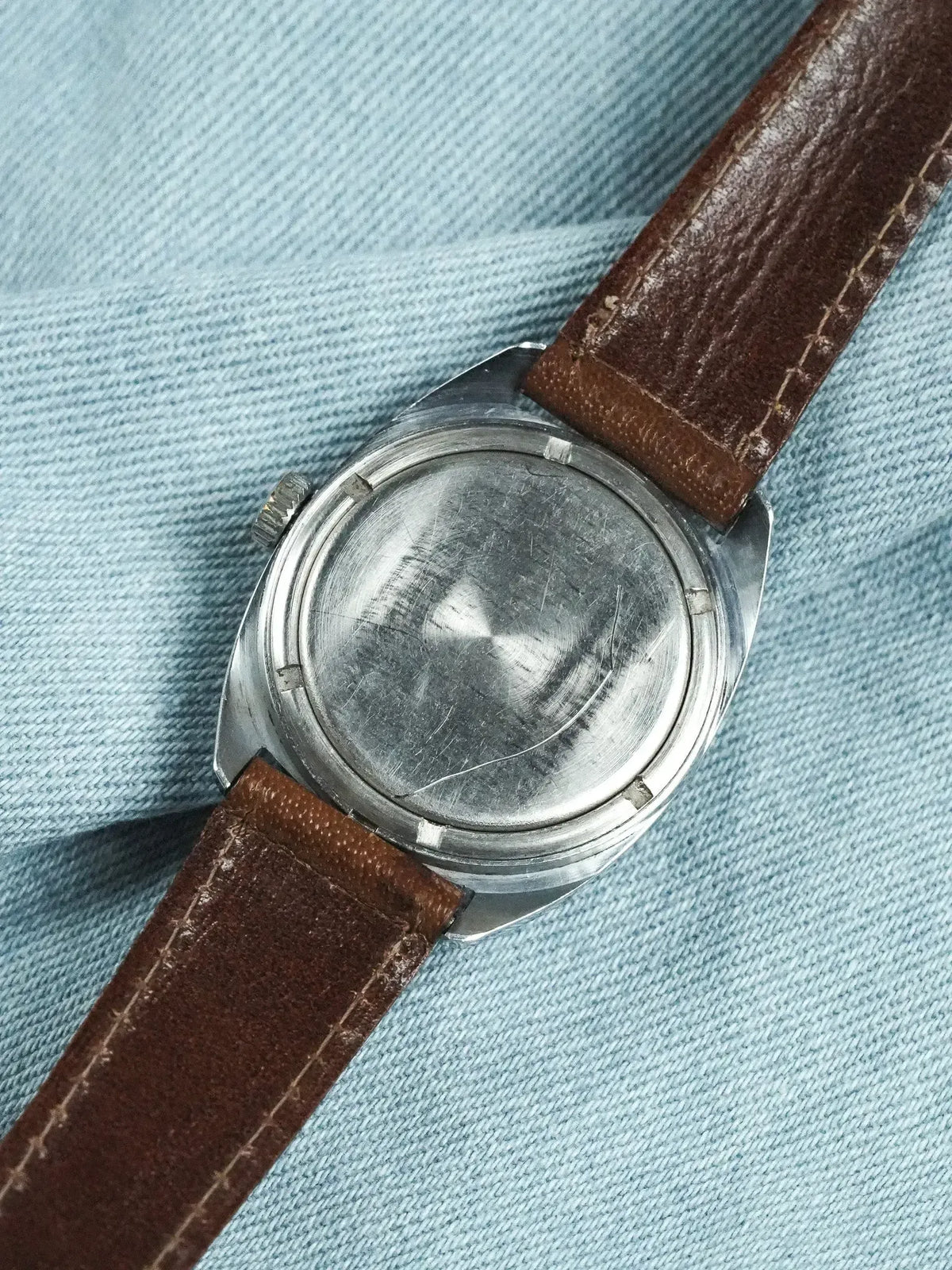 Vintage watch with steel case back and brown leather strap on denim