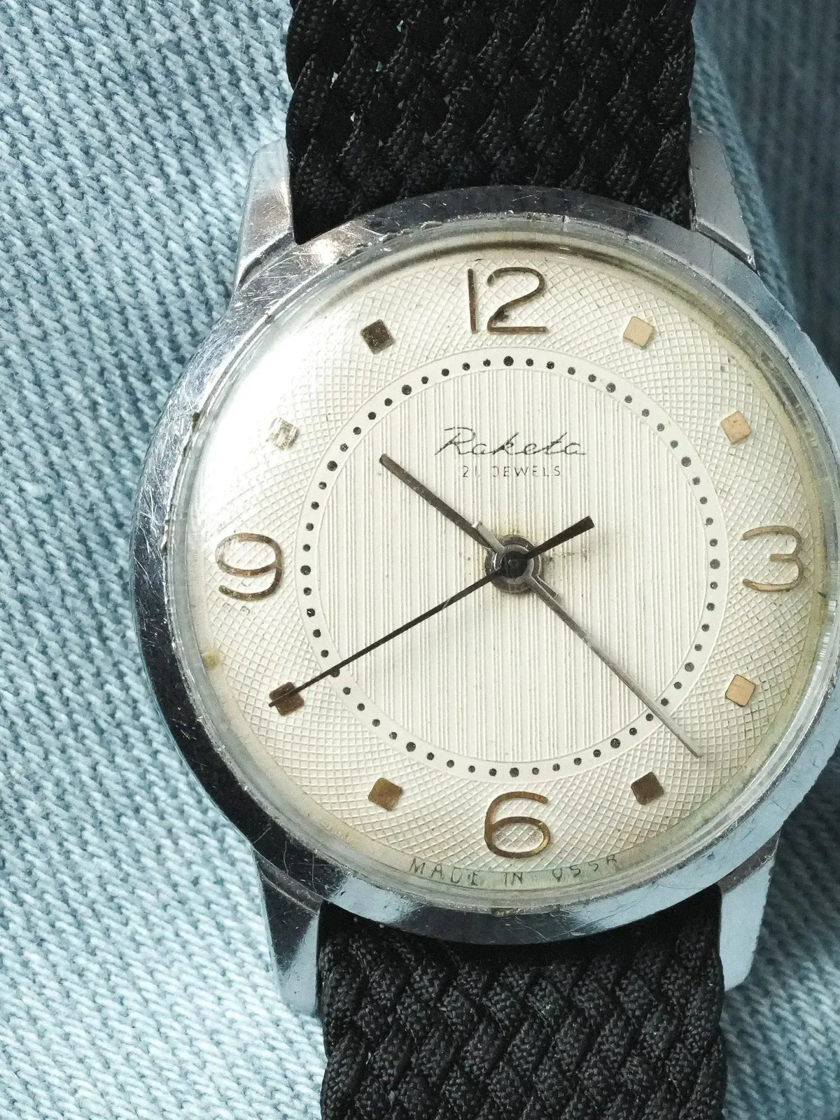 Raketa vintage watch with silver dial, black fabric strap, worn on denim