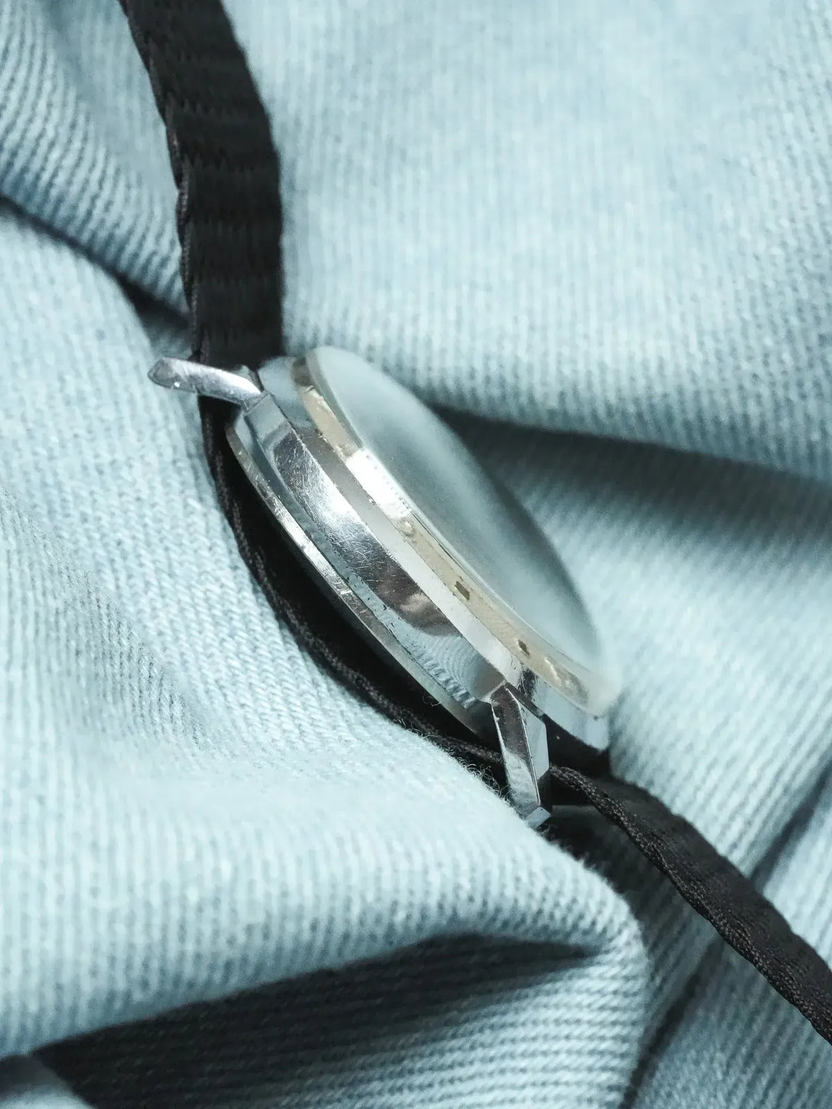 Vintage Omega watch side profile, stainless steel case, black fabric strap on light blue cloth