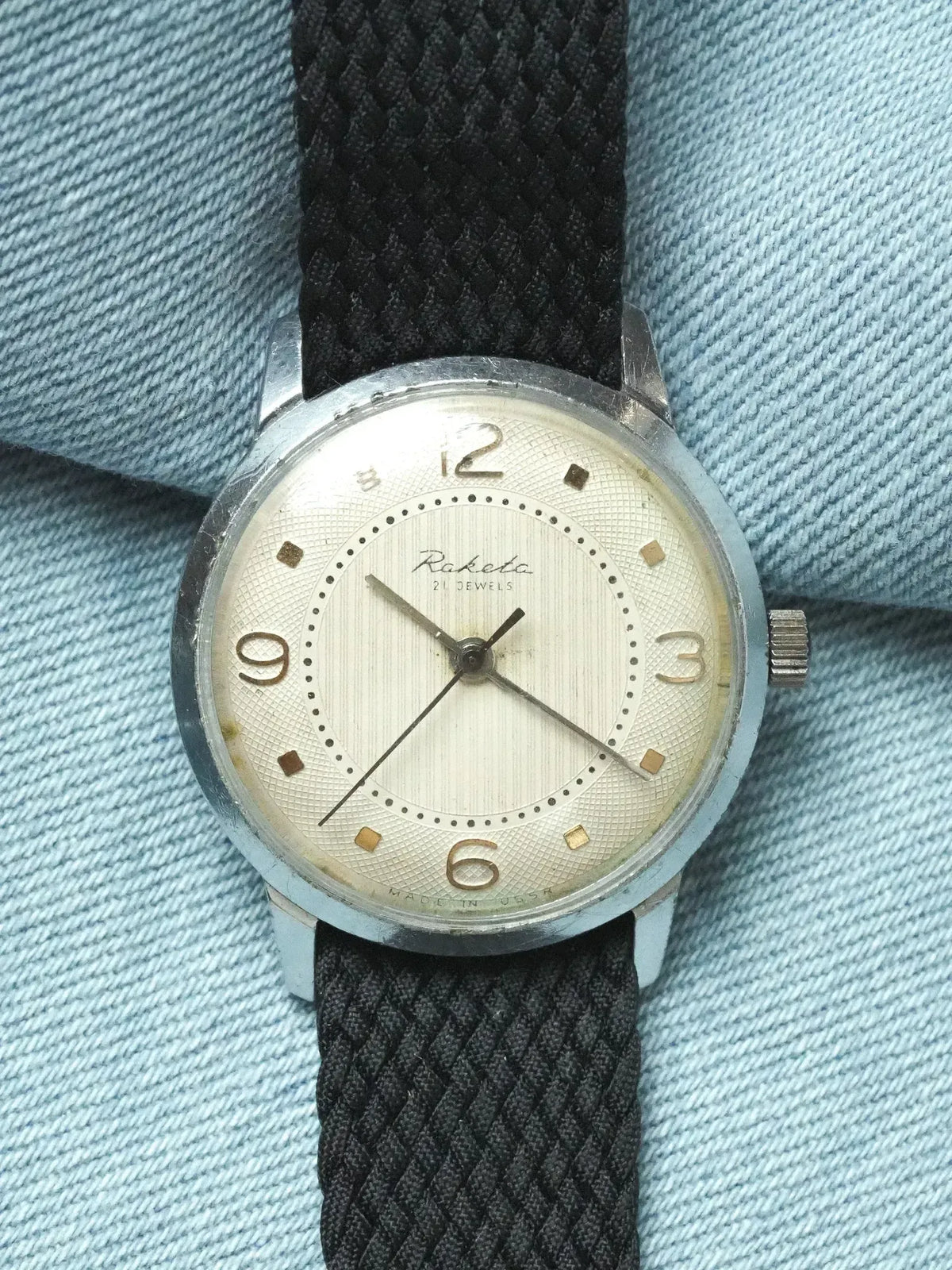 Raketa vintage watch with silver dial, black fabric strap, on denim background