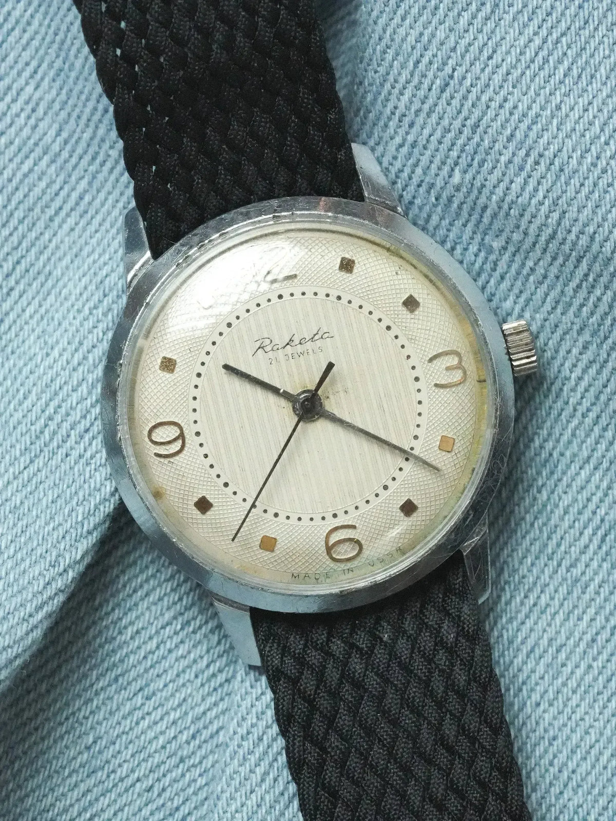 Raketa vintage watch with silver case, cream dial, black fabric strap on denim