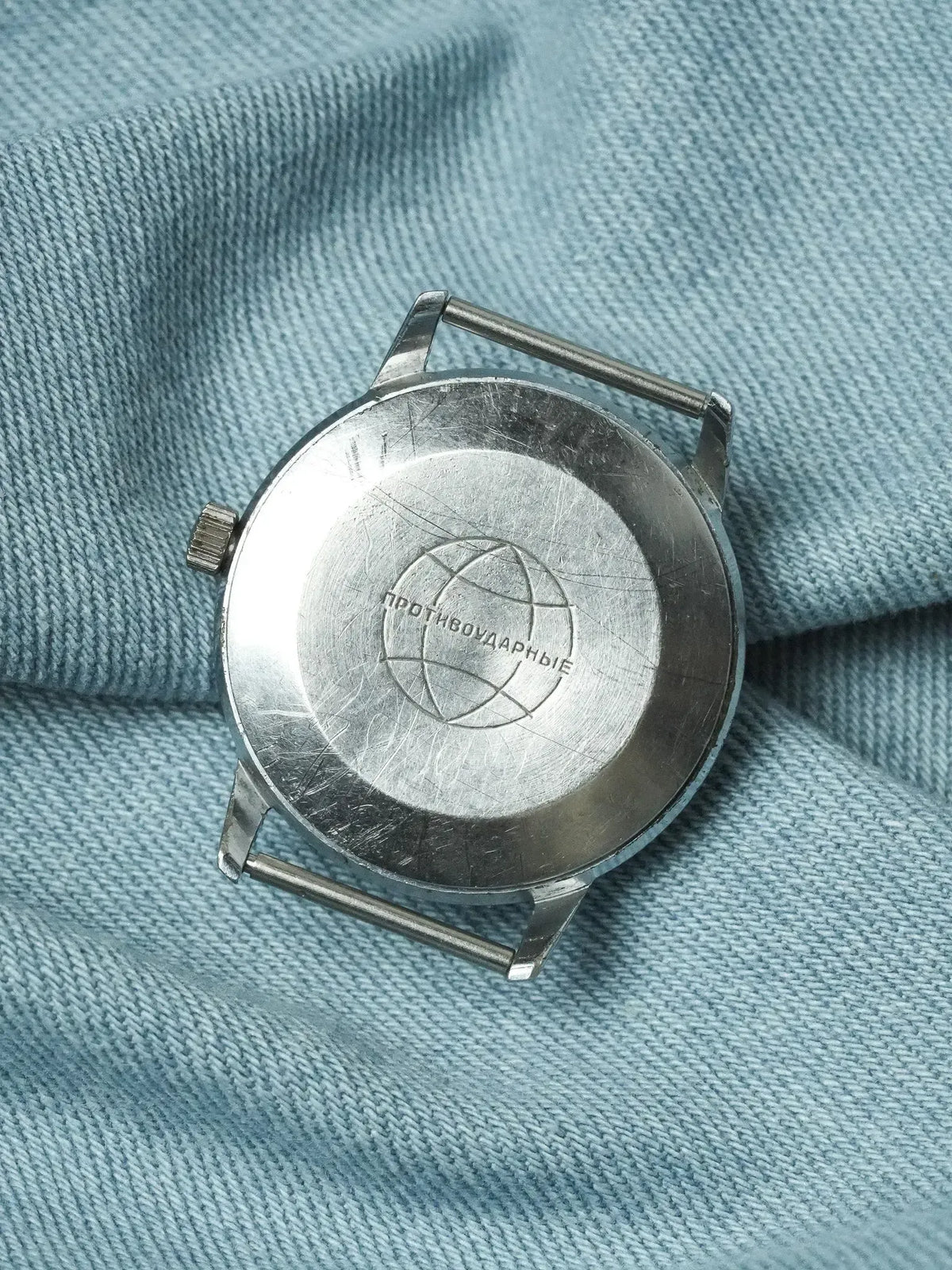 Vintage Soviet watch back with 'Противоударные' engraving, stainless steel case on blue fabric