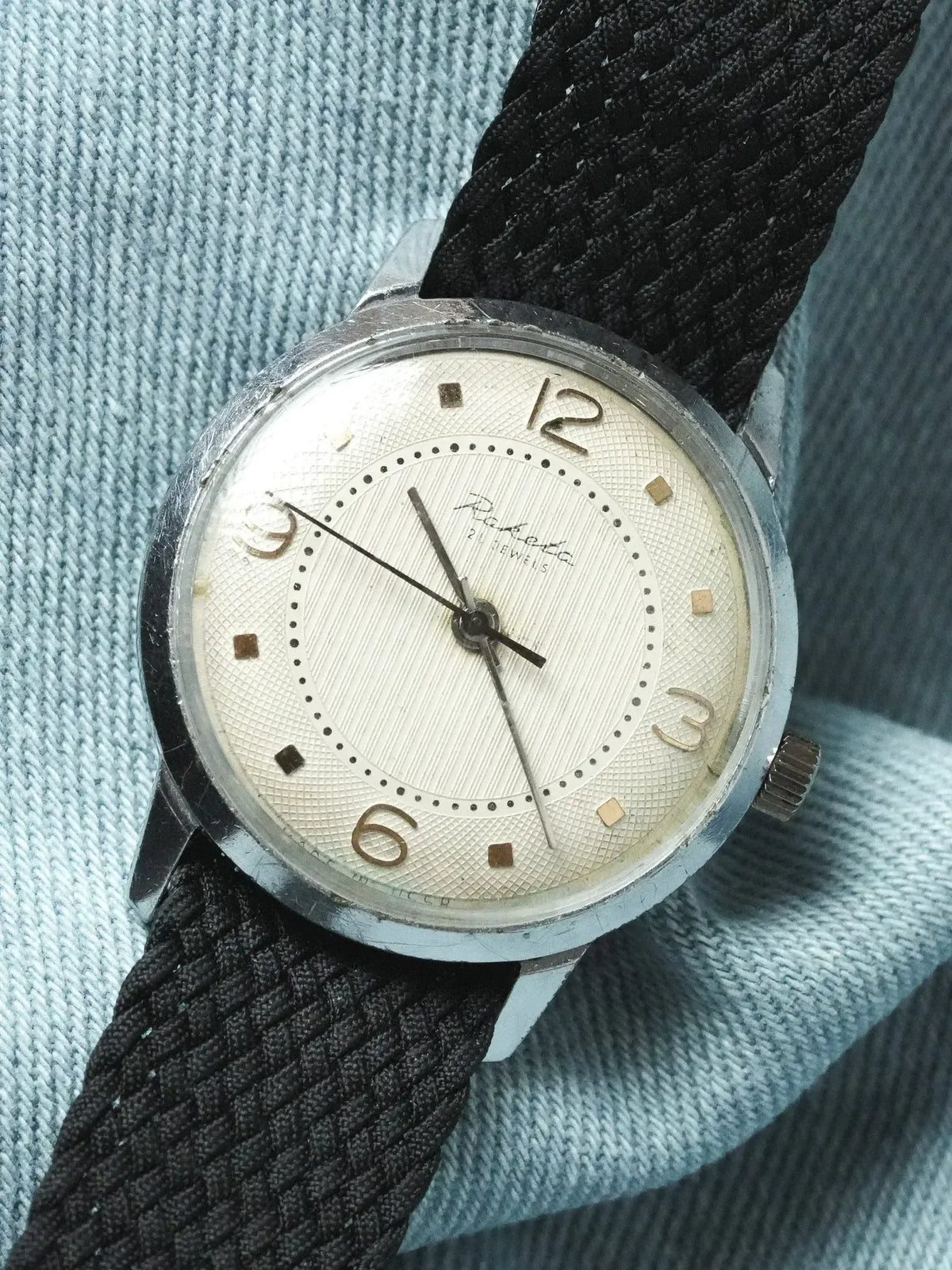 Raketa vintage watch with silver dial, black fabric strap, on denim background