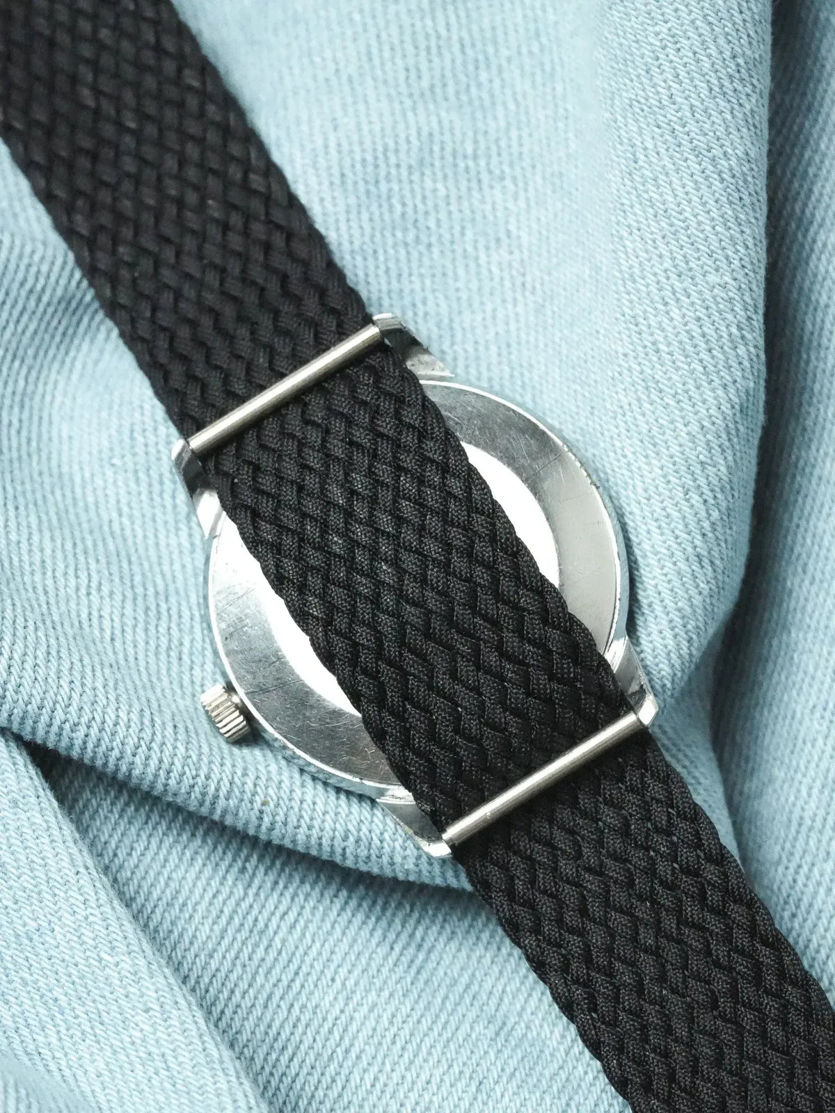 Vintage Omega watch with black braided strap on light blue fabric