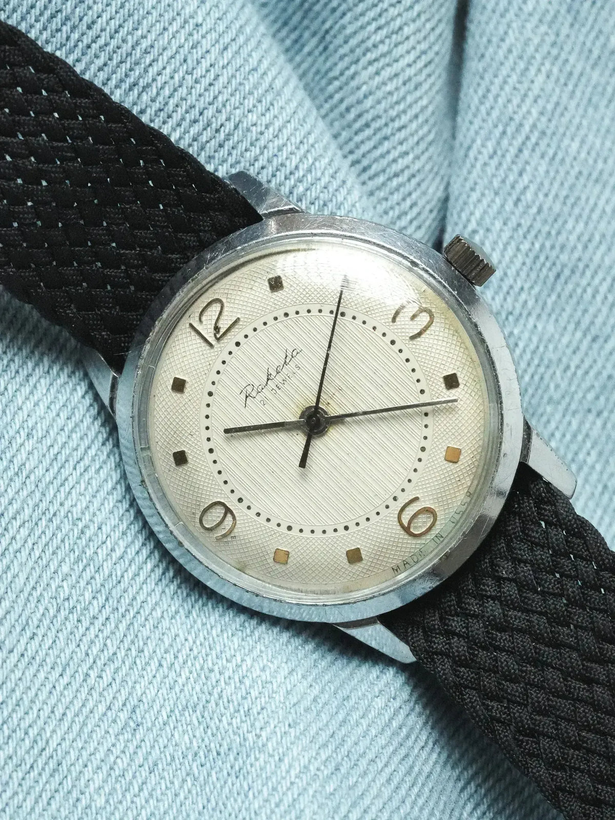 Raketa vintage watch with silver case, cream dial, black mesh strap on denim